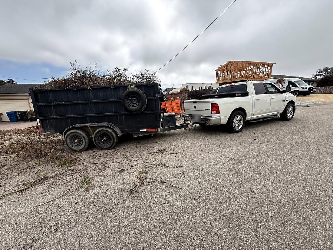 A dump trailer loaded with cut brush and debris, hitched behind the work truck